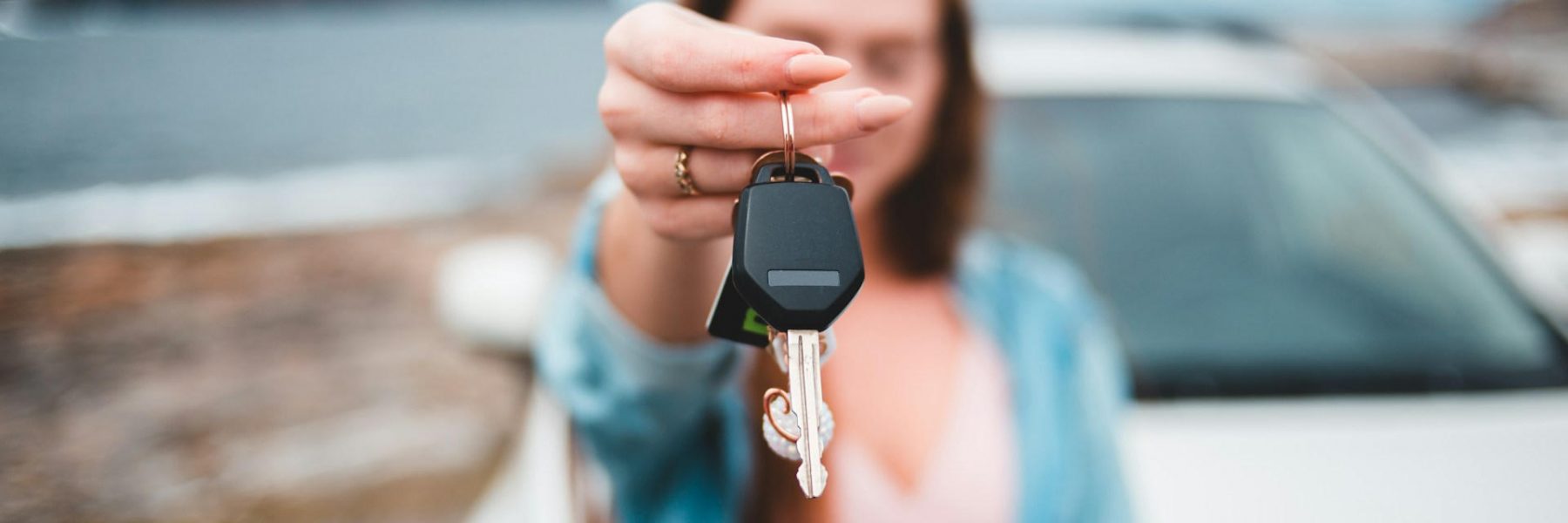 Une femme tend des clefs de voiture. La voiture est derrière elle. Les clefs sont nettes, tout l'arrière plan est flou.